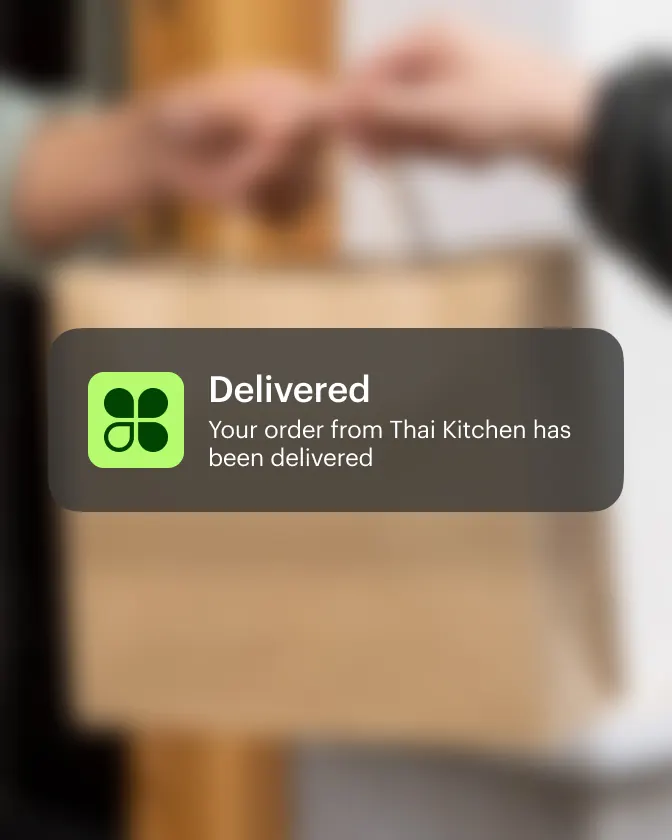 Hands passing a paper takeaway bag with a delivered-order notification card