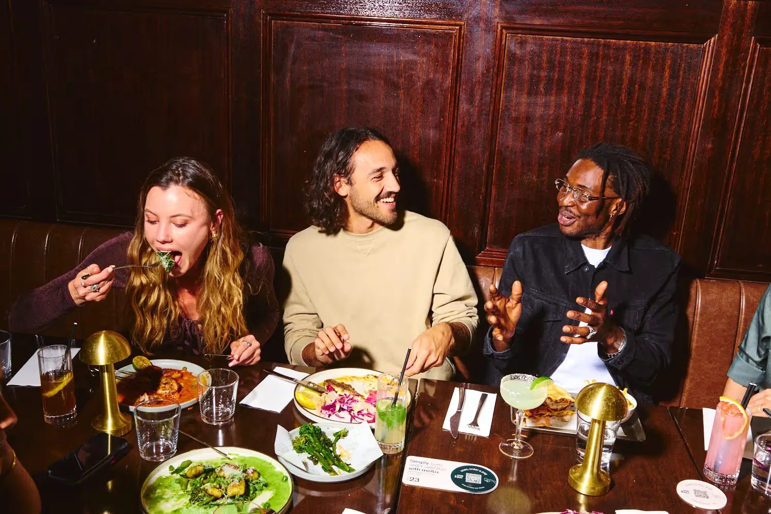 Three friends laughing and eating at a restaurant table