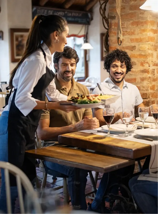 Waitress serving plates to two smiling diners at a restaurant table